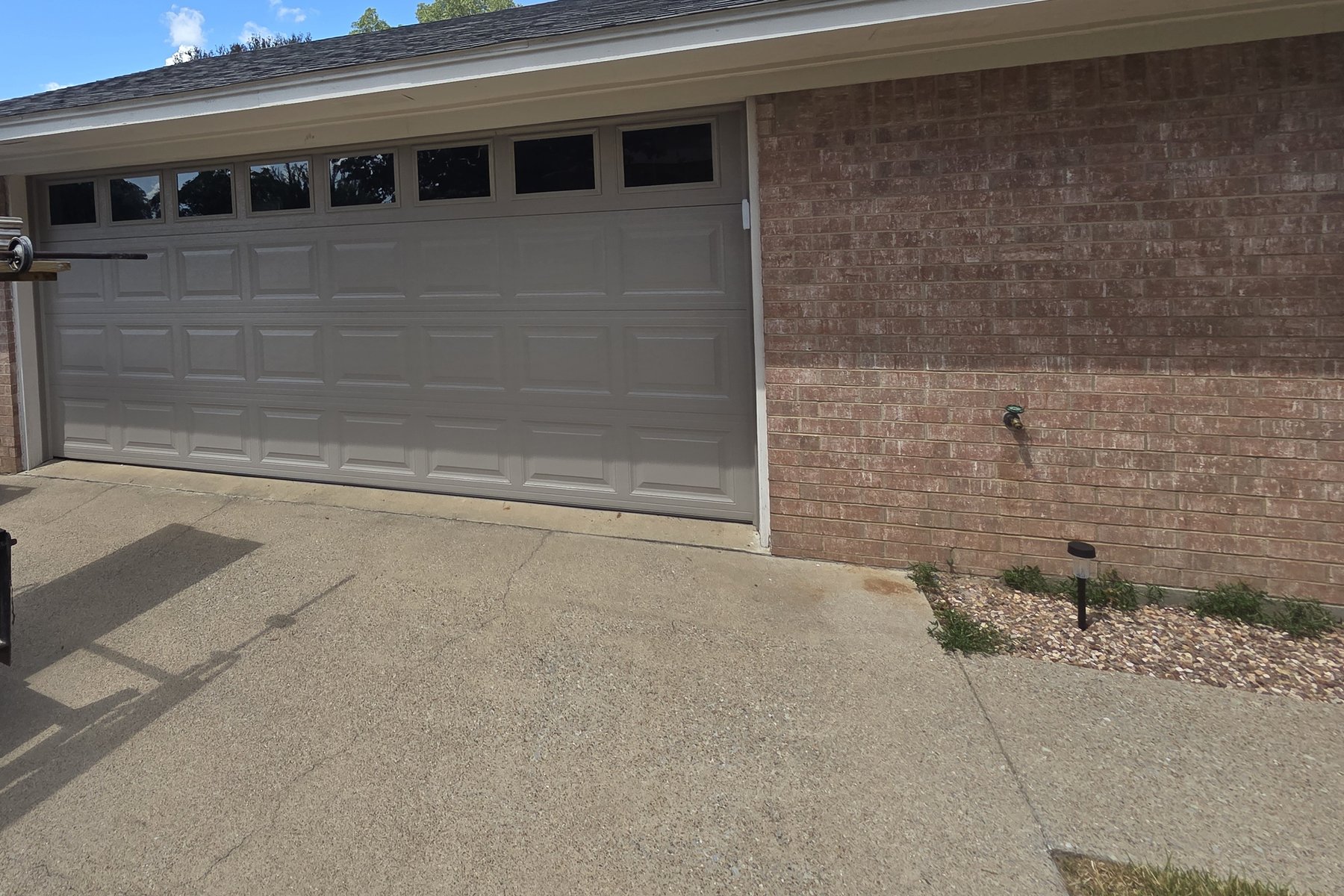 A tan raised-panel garage door with a row of windows across the top