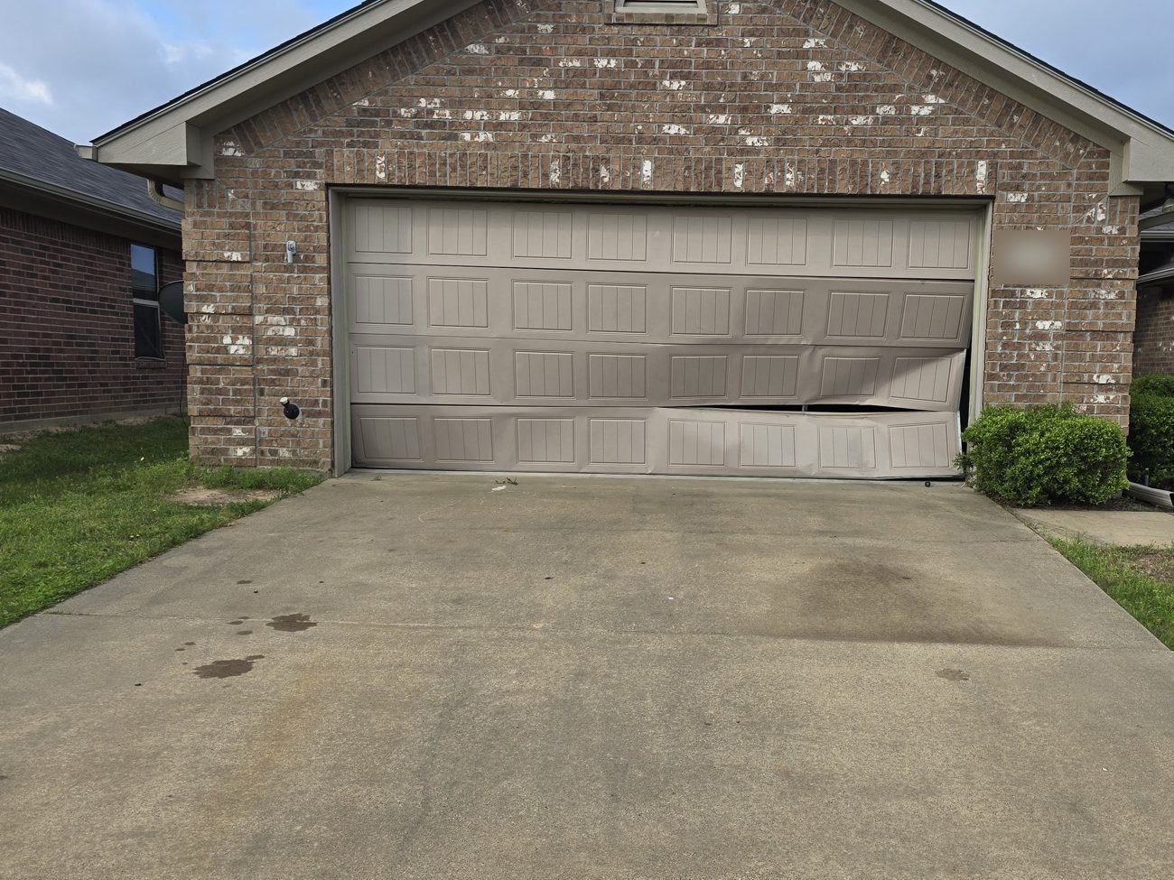 A garage door bent and pulled off its track on a brick house
