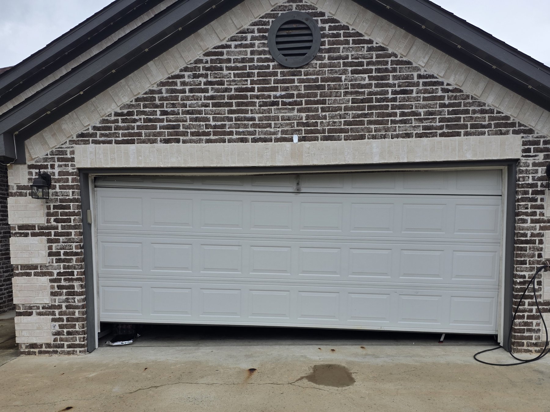 A white garage door hanging crooked and off its track on a brick house